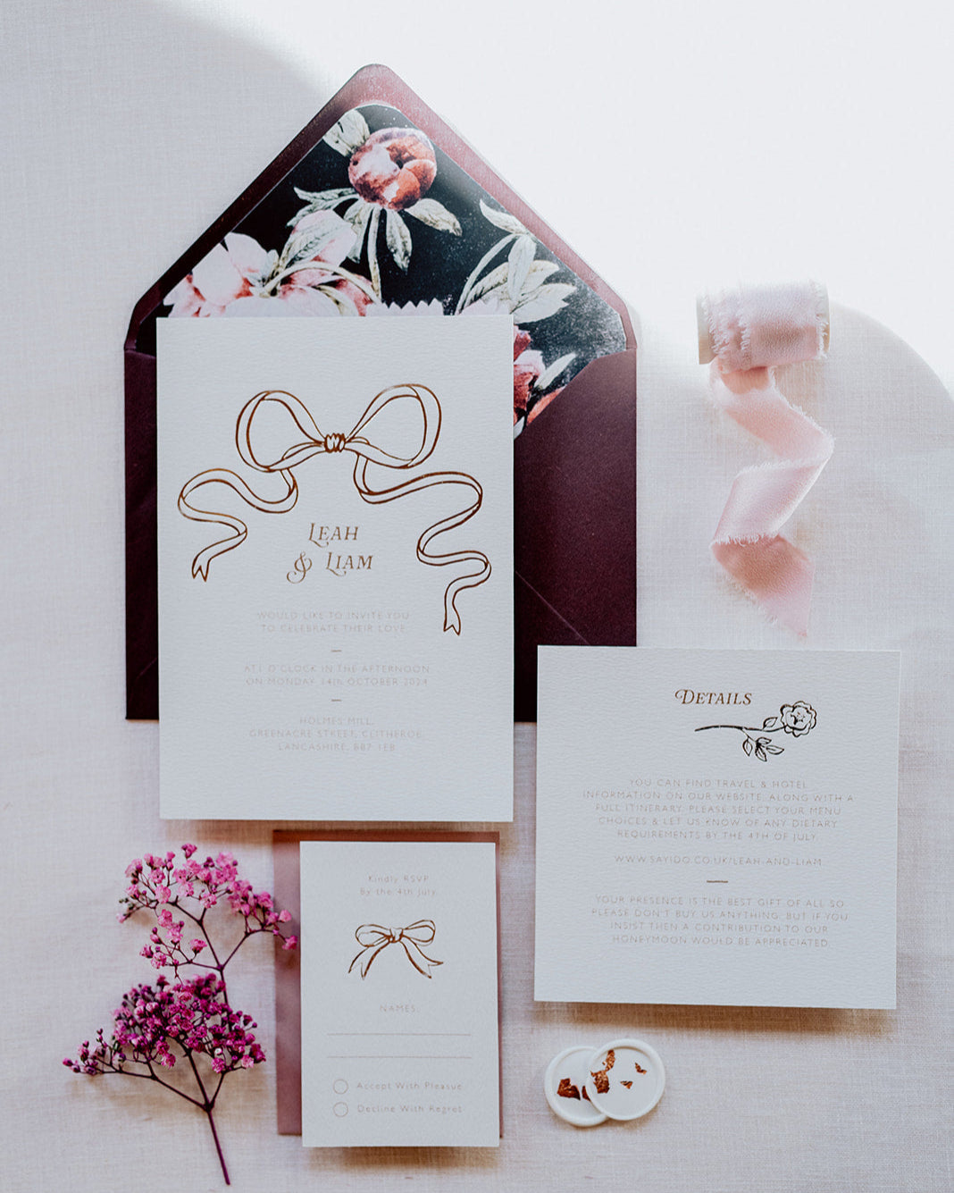 Wedding Invitation Sample Pack featuring a large Rose Gold Bow Design, foiled onto thick textured card with couples names and information printed in a soft brown colour. Paired with burgundy envelope with floral envelope liner, white wax seal with rose gold flakes and blush pink silk ribbon. Laid out flat lay style with Details card and RSVP. Designed by Fancy Folk Wedding Stationery
