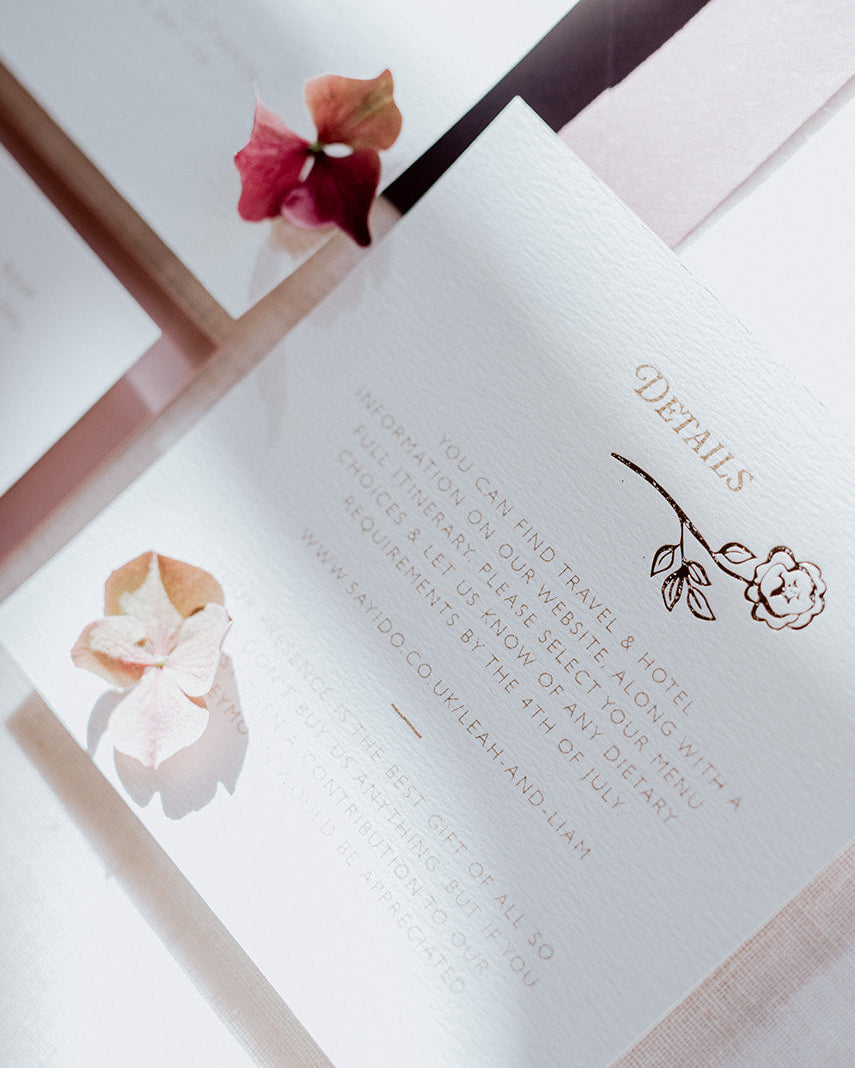 Close up of wedding details card featuring a foiled rose steam deign below the word 'Details'. Foiled onto thick textured card with couples information printed in a soft brown colour. Designed by Fancy Folk Wedding Stationery