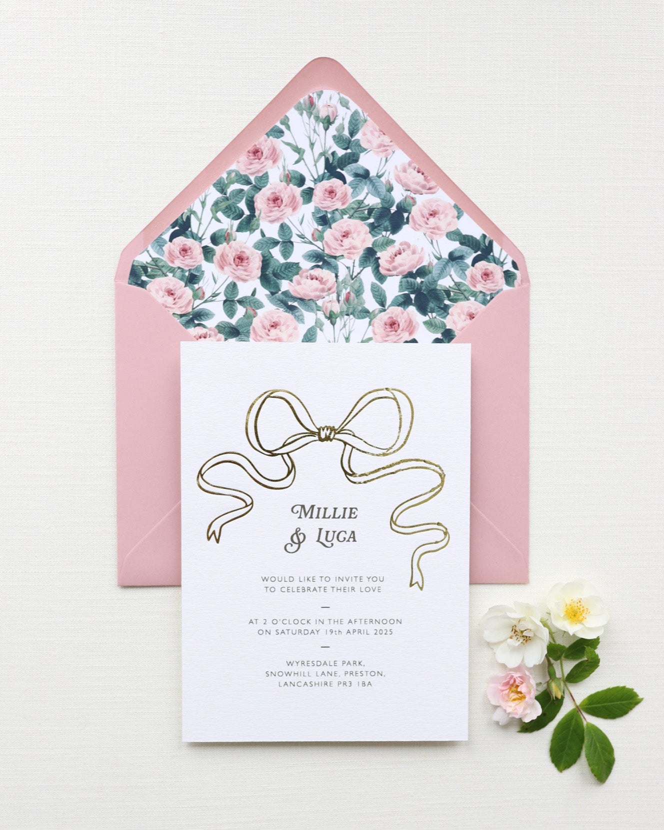 Bow Wedding Invitation featuring a large Gold Bow Design, foiled onto thick textured card with couples names and information printed in a soft brown colour. Paired with dusky pink envelope with english rose garden floral envelope liner. Designed by Fancy Folk Wedding Stationery