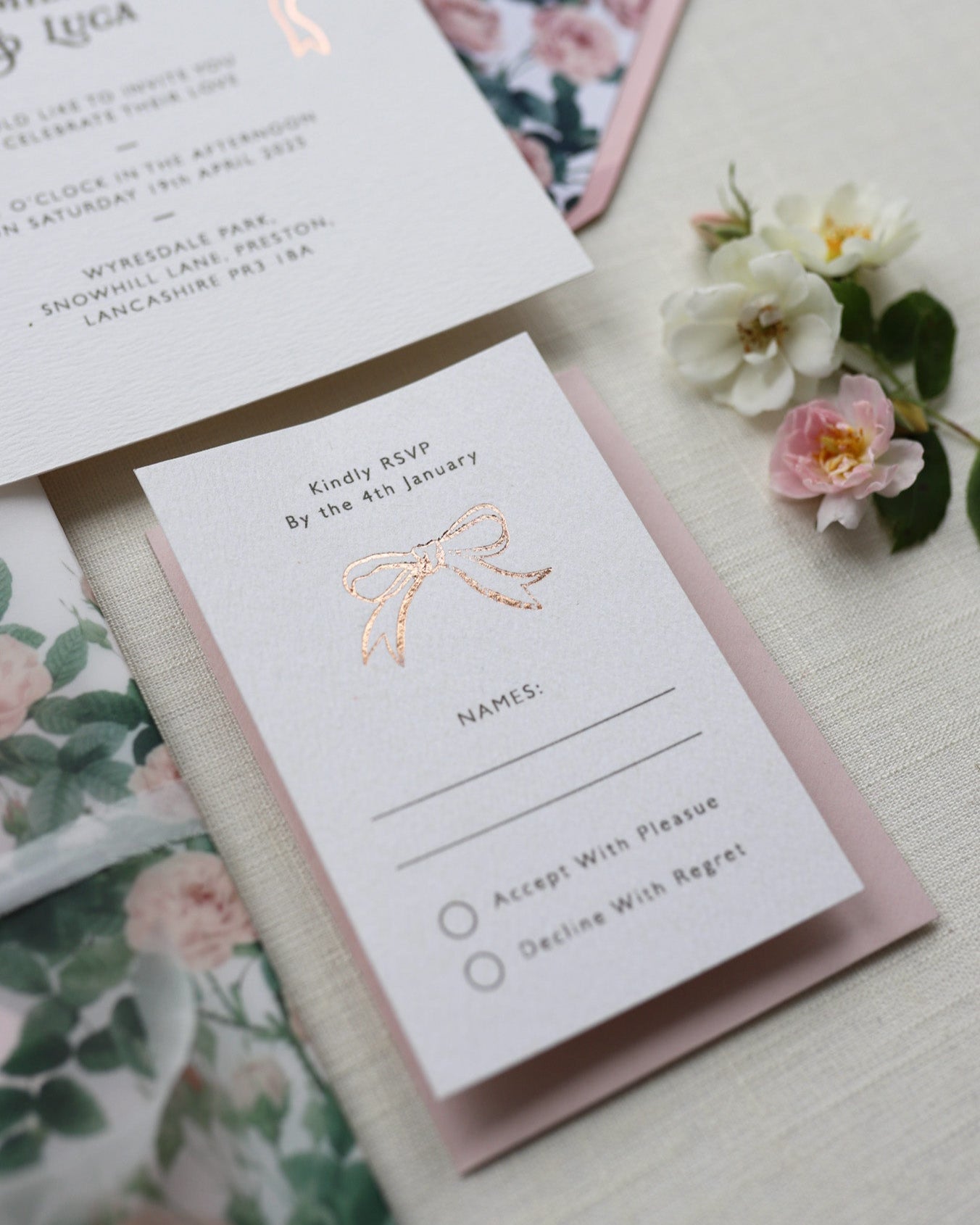 Bow Wedding RSVP featuring a small Rose Gold Bow Design, foiled onto thick textured card with couples names and information printed in a soft brown colour. Paired with dusky pink envelope. Designed by Fancy Folk Wedding Stationery