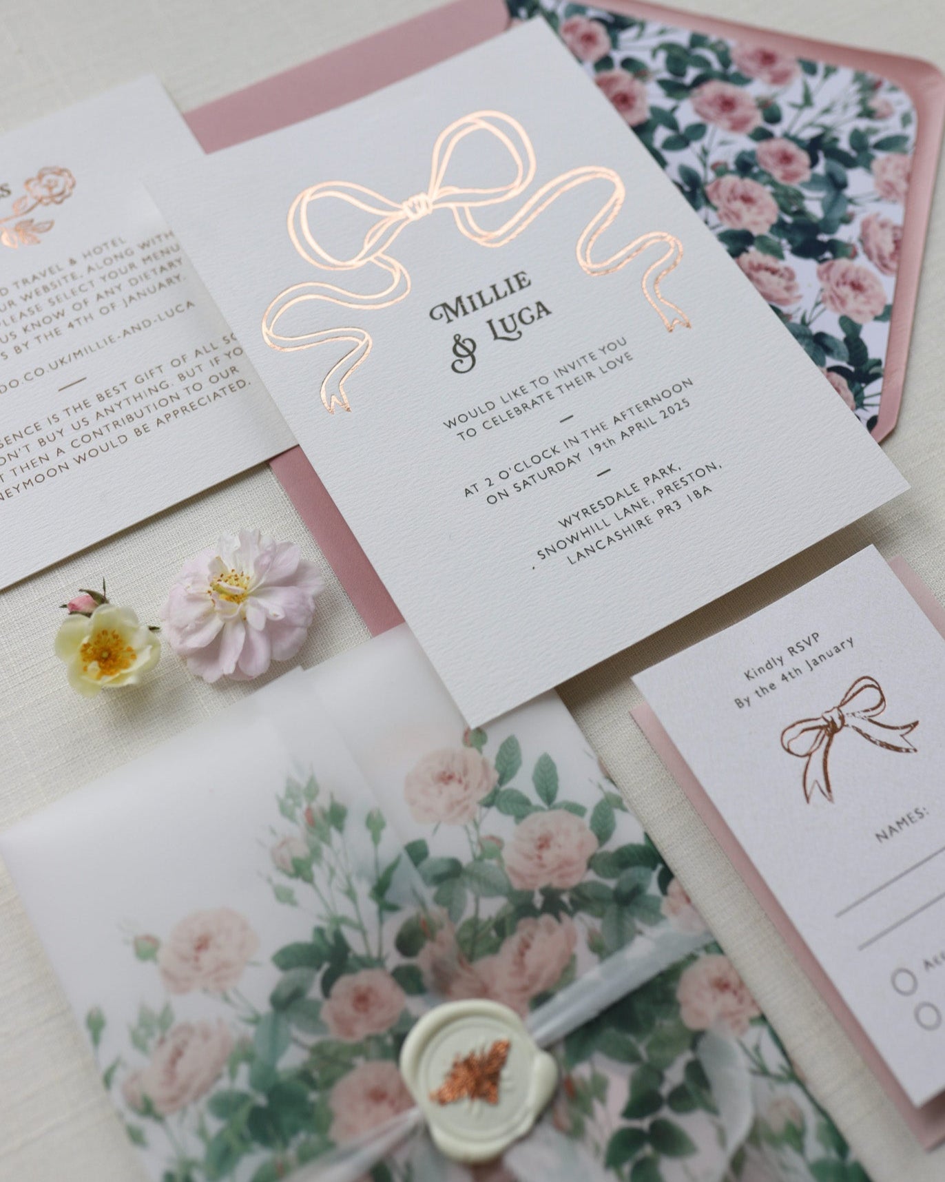 Bow Wedding Invitation featuring a large Rose Gold Bow Design, foiled onto thick textured card with couples names and information printed in a soft brown colour. Paired with dusky pink envelope with english rose garden floral envelope liner. Laid out flat lay style with Details card and RSVP and wild roses. Designed by Fancy Folk Wedding Stationery