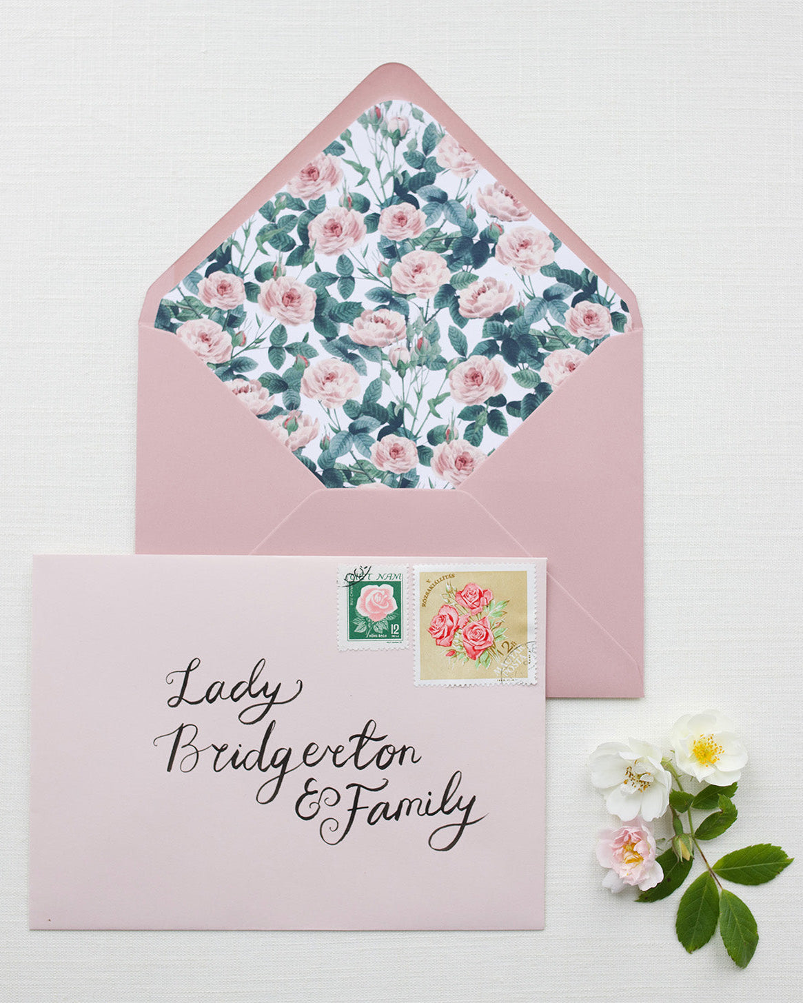 Hand Calligraphy Address written on a blush pink envelope. It reads "Lady Bridgerton & Family" styled with pink rose garden envelope liner. Fancy Folk Wedding Stationery