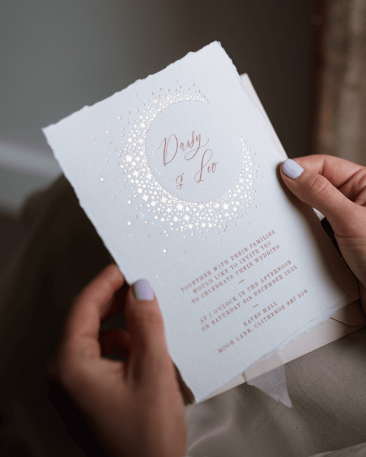 Celestial themed wedding invitation being opened by a lady. A truly magical crescent moon design made up of lots of little stars is hot foiled in gold on to tactile handmade paper with a torn romantic edge. The gold foil sparkles in the light. FancyFolk Design