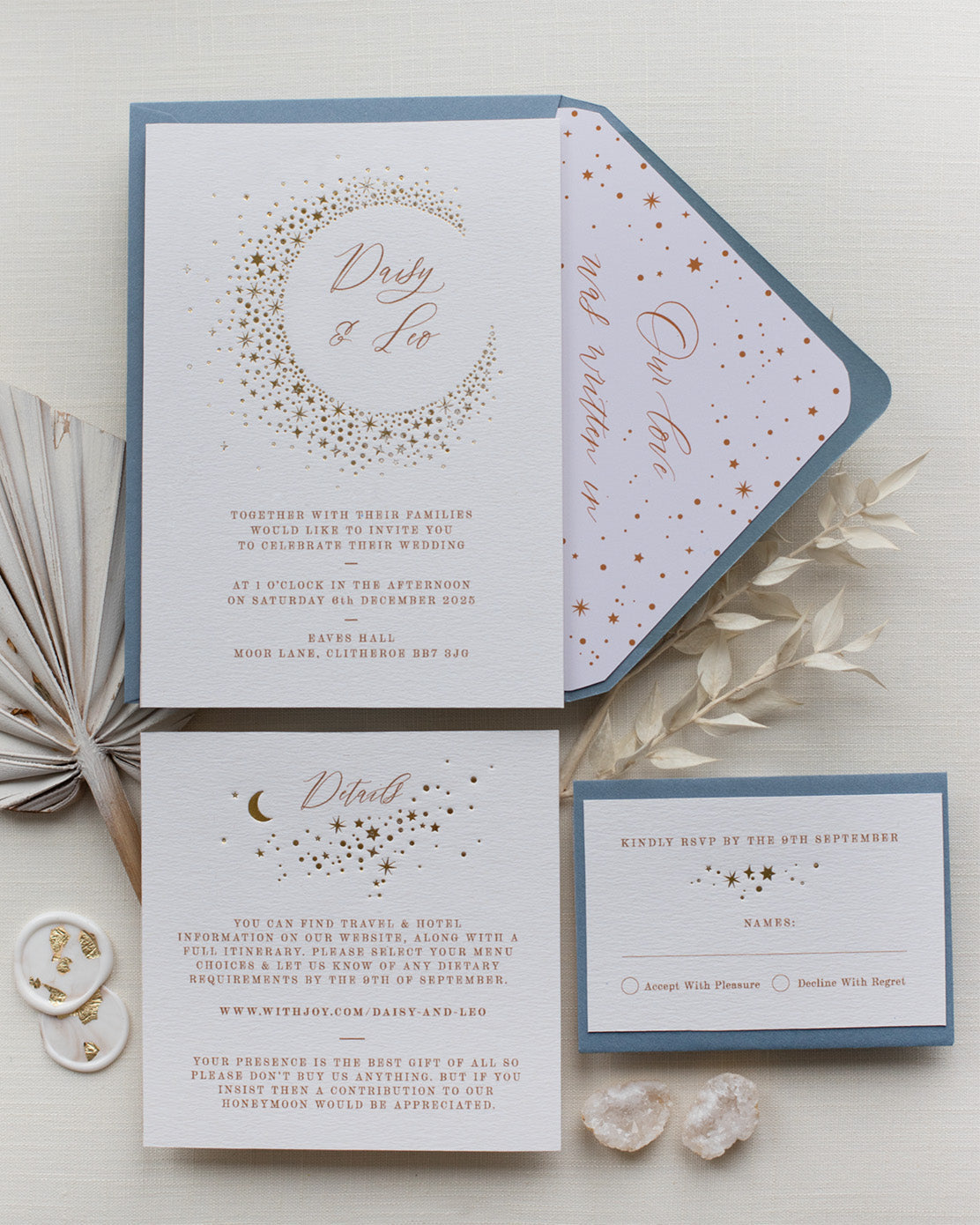 Celestial themed wedding stationery suite laid out in a flat lay format. A truly magical crescent moon design made up of lots of little stars is hot foiled in gold on to the main invitation. Smaller cluster of gold stars feature on the details card and RSVP. The invitations are foiled and printed onto thick textured card, styled with silk ribbon, wax seals and dusty blue coloured envelopes. FancyFolk Design