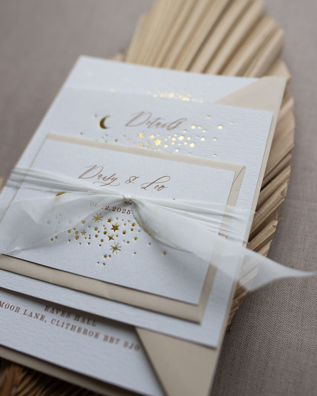 Celestial wedding stationery sample pack. Invitation,Details card and RSVP layer on top of each other, tied together in a perfect bundle with white silk ribbon. A truly magical crescent moon design made up of lots of little stars is hot foiled in gold on to the main invitation. Smaller cluster of gold stars feature on the details card and RSVP. The invitations are foiled and printed onto thick textured card, styled with silk ribbon, wax seals and almond coloured envelopes. FancyFolk Design