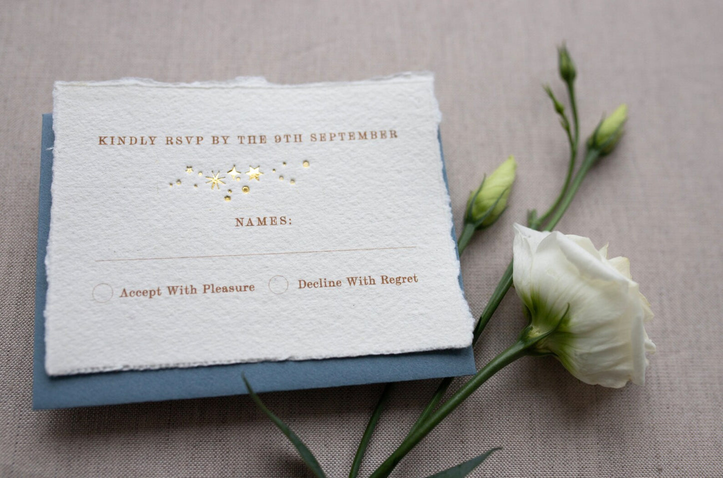 Celestial wedding RSVP card. Spakley scatter of gold foiled stars with printed words reading "Kindly RSVP" Followed by your details. Printed onto handmade paper with romantic torn edges. Styled with a duty blue envelope. Fancy Folk
