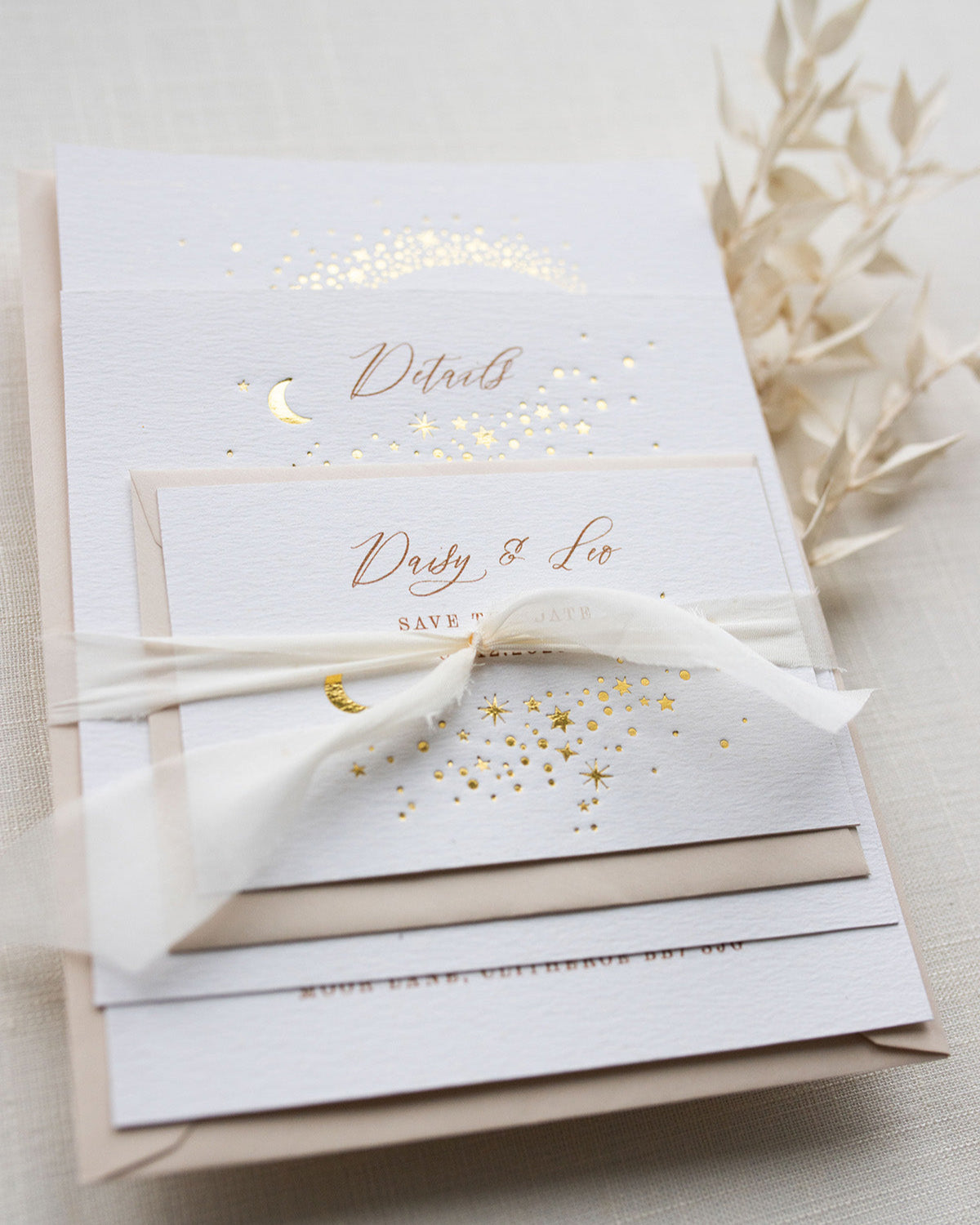 Celestial wedding stationery sample pack. Invitation,Details card and RSVP layer on top of each other, tied together in a perfect bundle with white silk ribbon. A truly magical crescent moon design made up of lots of little stars is hot foiled in gold on to the main invitation. Smaller cluster of gold stars feature on the details card and RSVP. The invitations are foiled and printed onto thick textured card, styled with silk ribbon, wax seals and almond coloured envelopes. FancyFolk Design