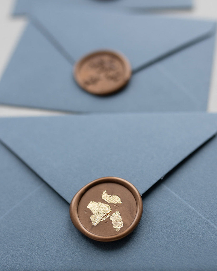 Gold Wax Seal with shiny gold leaf flakes pressed into it. Placed on a dusty blue envelope. Fancy Folk Design