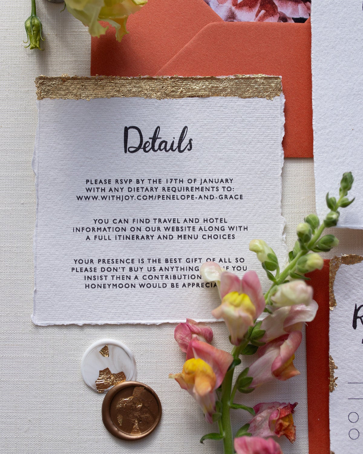 Modern Calligraphy Wedding Details Card with terracotta coloured envelopes. Our wedding stationery features a beautiful hand lettered calligraphy names design printed on textured handmade Indian paper with hand torn edges for a soft romantic feel. Each piece is lovingly hand finished with gold leaf for a luxury feel. Styled with white and gold leaf wax seals and peachy florals. Fancy Folk