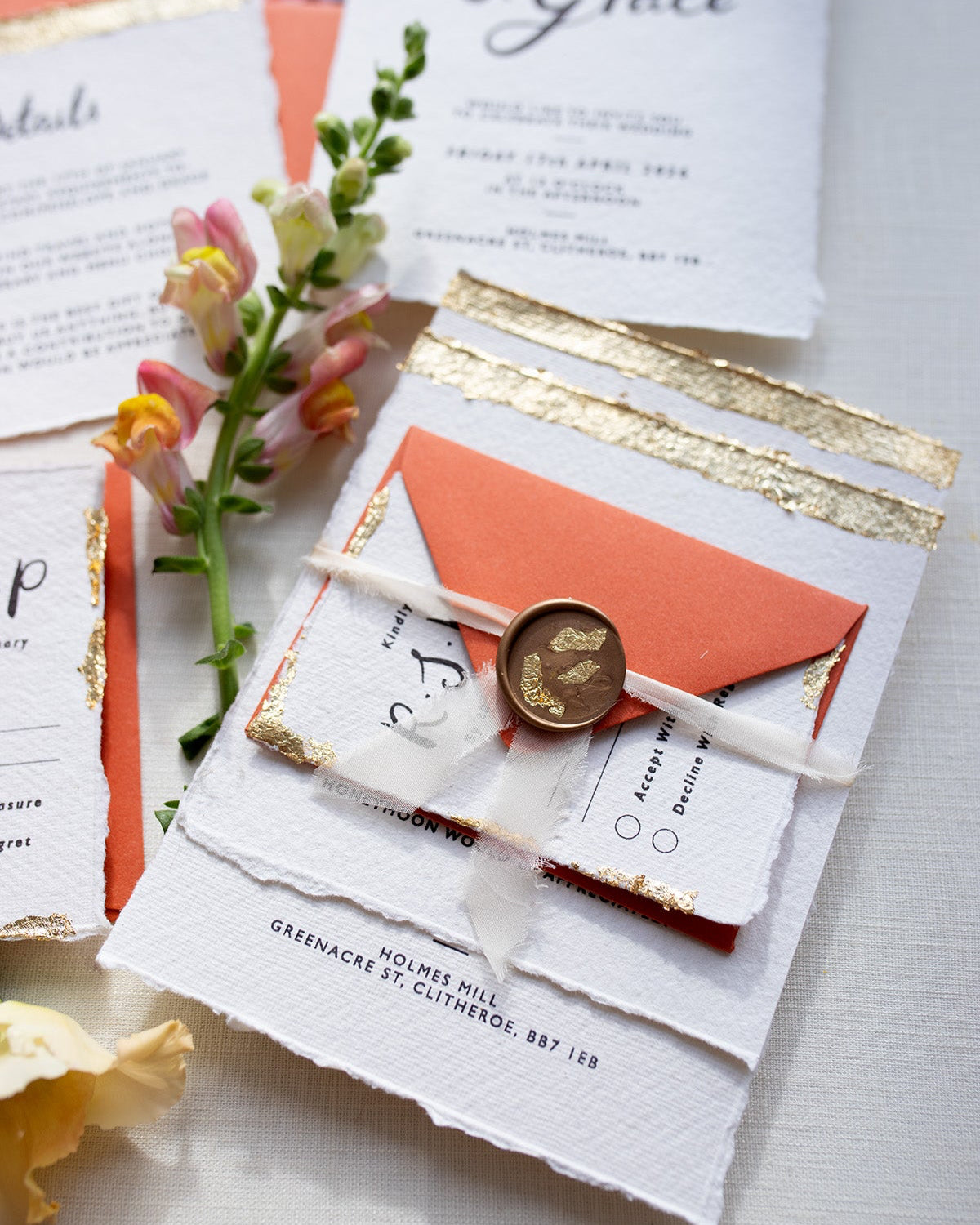 Modern Calligraphy Wedding Sample pack. Includes Invitation, Details card, RSVP with terracotta coloured envelopes, wax seal and silk ribbon. Our wedding stationery features a beautiful hand lettered calligraphy names design printed on textured handmade Indian paper with hand torn edges for a soft romantic feel. Each piece is lovingly hand finished with gold leaf for a luxury feel. Styled with white and gold leaf wax seals and peachy florals. Fancy Folk