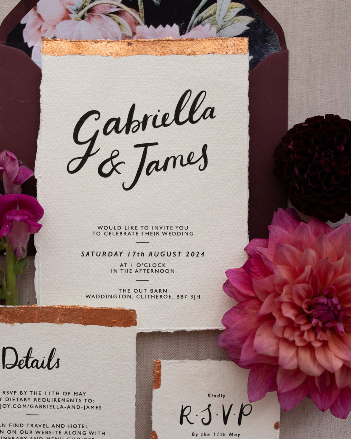 Close up of a Modern Calligraphy Wedding Invitation, Details Card and RSVP with rich burgundy coloured envelopes. Our wedding stationery features a beautiful hand lettered calligraphy names design printed on textured handmade Indian paper with hand torn edges for a soft romantic feel. Each piece is lovingly hand finished with copper leaf for a luxury feel. Styled with burgundy and coral florals, perfect for autumn and winter weddings. Fancy Folk