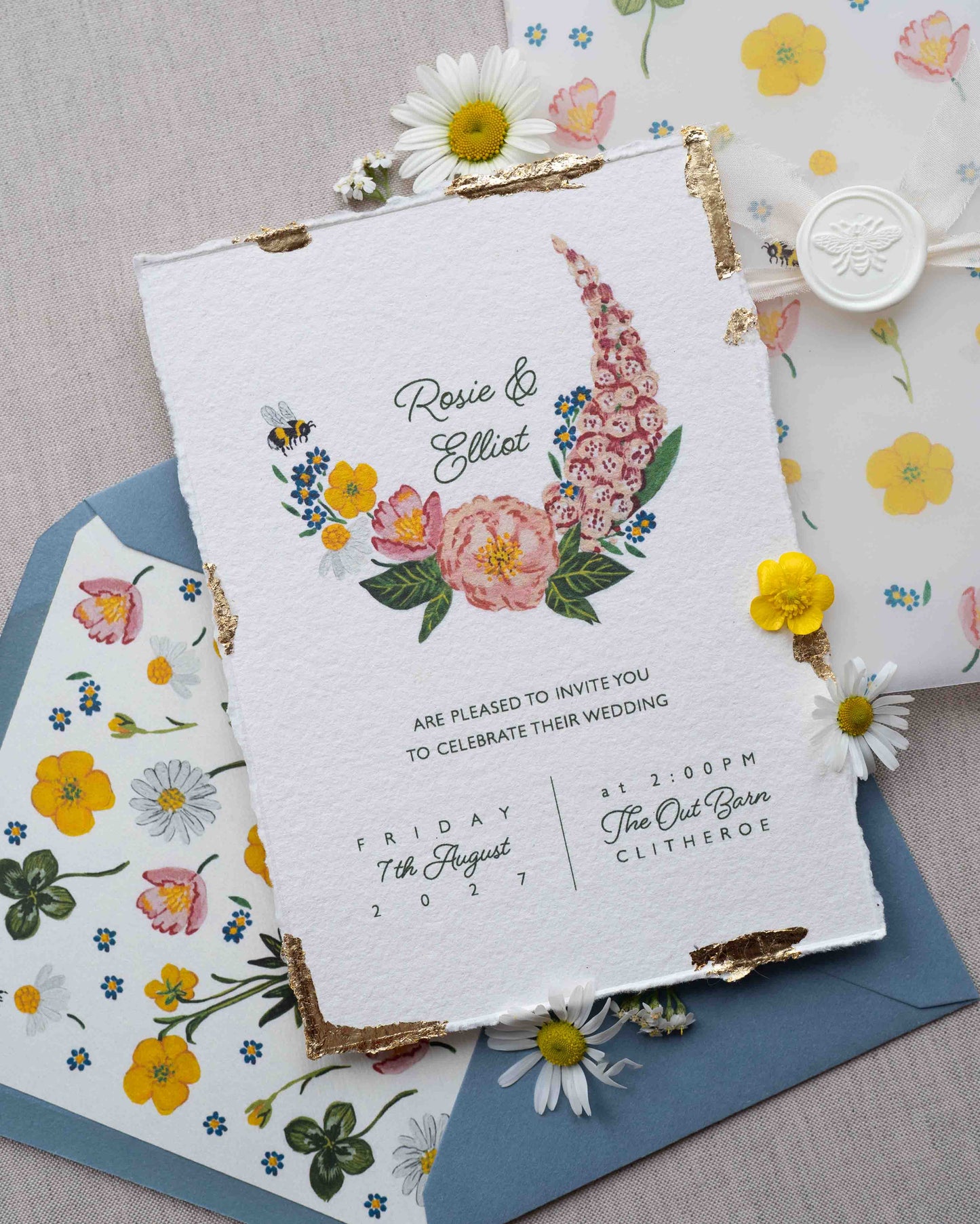 Watercolour hand painted florals of meadow flowers and a little bee make up a posy. Couples names are nestled in the floral. Printed on handmade Indian cotton paper with gold leaf accent. Styled with white bee wax seals, floral envelope liners and silk ribbon. Dusty blue envelopes and floral vellum wrap.