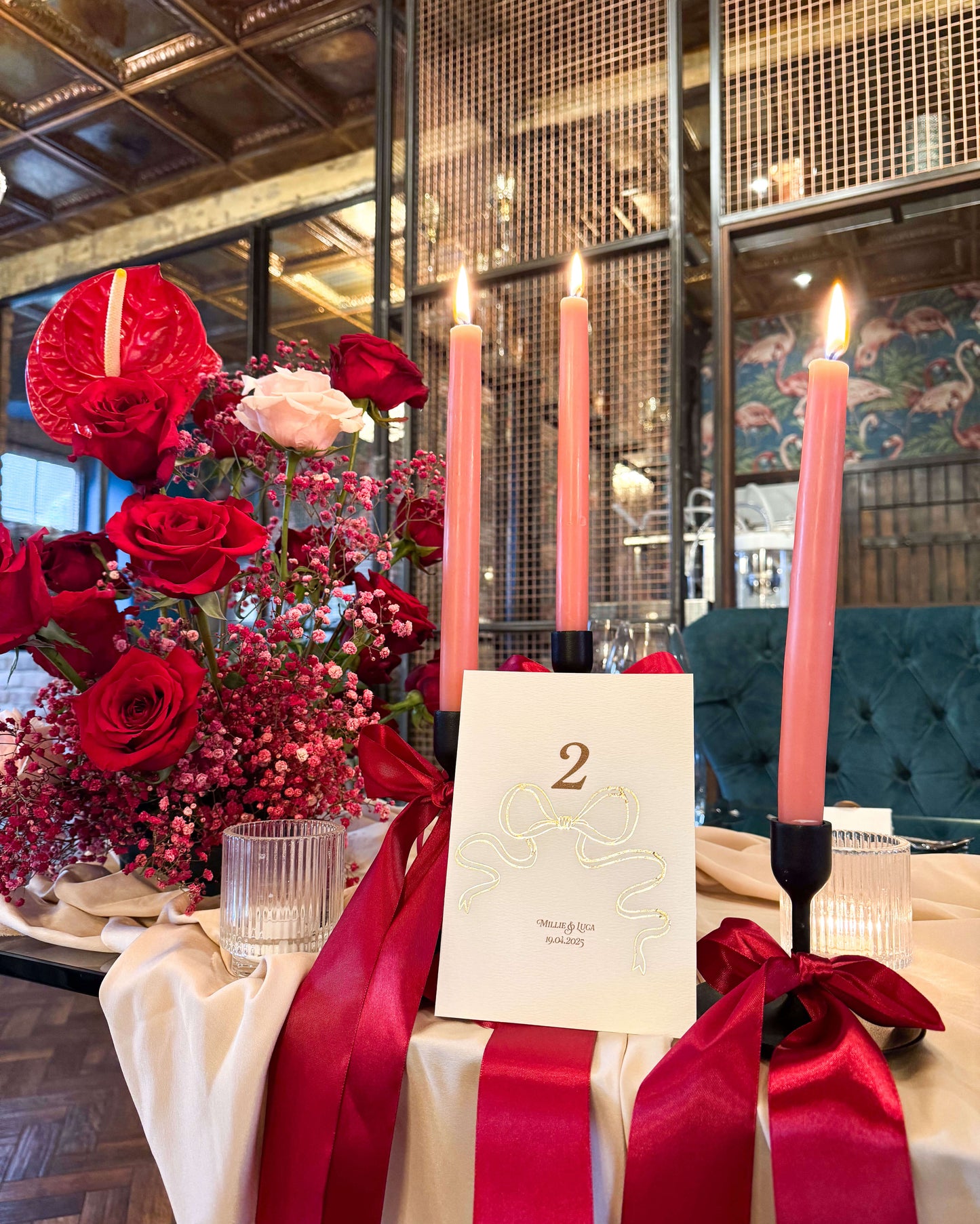 Gold Foil Bow design Wedding Table Numbers with printed couples names and wedding date. Styled with red florals and large satin Bow candle stick Designed by Fancy Folk Wedding Sationery.