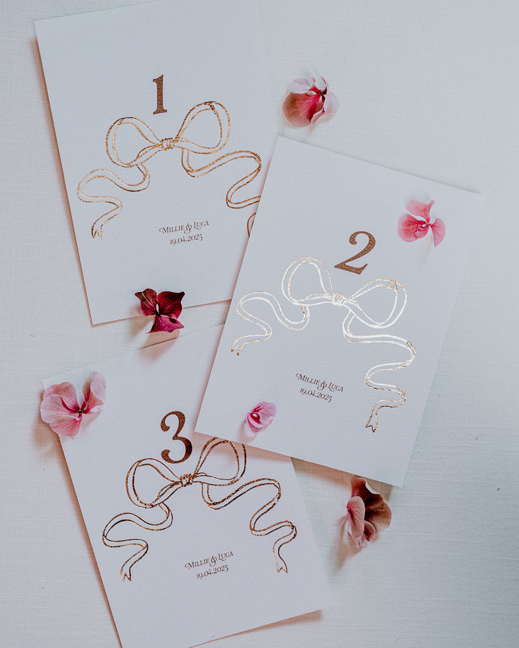 Rose Gold Foil Bow design Wedding Table Numbers with printed couples names and wedding date. Designed by Fancy Folk Wedding Sationery.