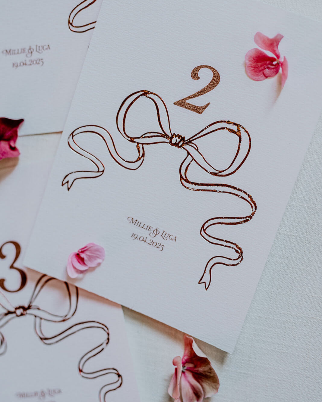 Close up of Rose Gold Foil Bow design Wedding Table Numbers with printed couples names and wedding date. Designed by Fancy Folk Wedding Sationery.