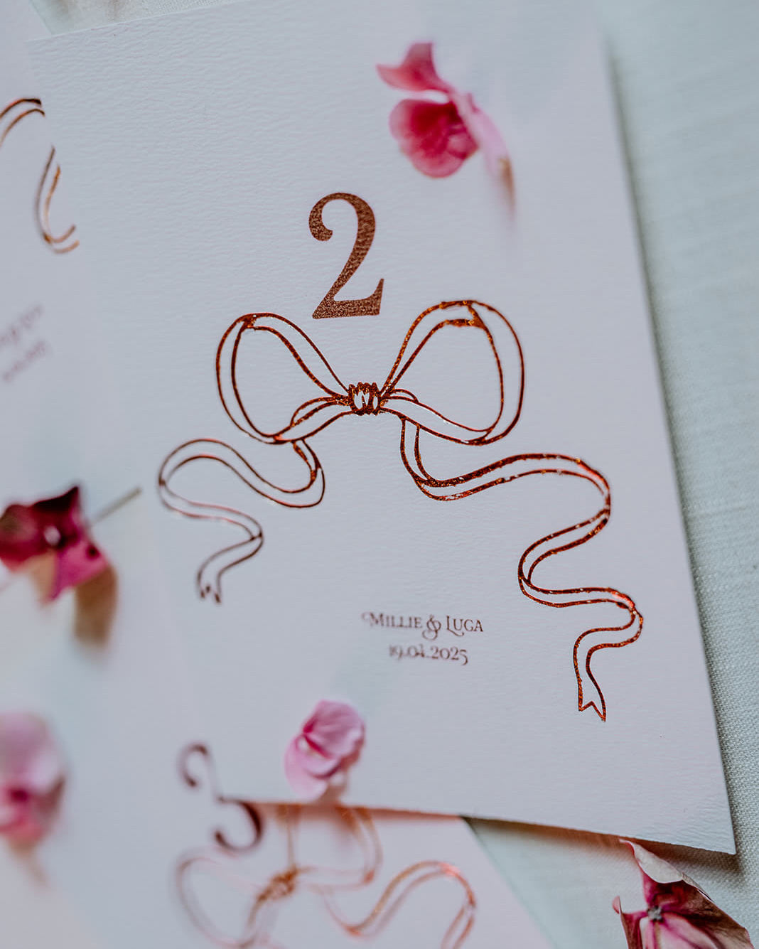 Close up of Rose Gold Foil Bow design Wedding Table Numbers with printed couples names and wedding date. Designed by Fancy Folk Wedding Sationery