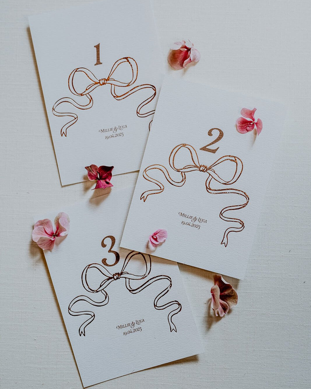 Rose Gold Foil Bow design Wedding Table Numbers with printed couples names and wedding date. Designed by Fancy Folk Wedding Sationery