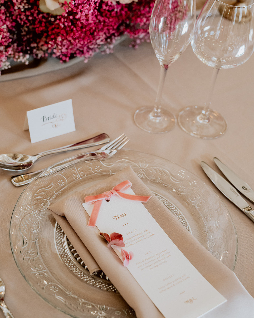 Blush velvet bow wedding breakfast menu place on a neutral napkin with hot pink floral arrangment on the table. Designed by Fancy Folk Wedding Stationery.