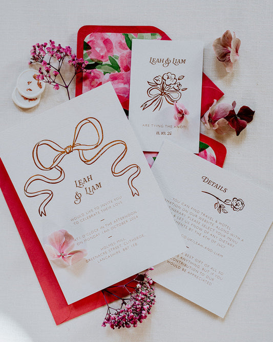 Bow Wedding Invitation featuring a large Rose Gold Bow Design, foiled onto  thick textured card with couples names and information printed in a soft brown colour. Paired with hot pink envelope with floral envelope liner, white wax seal with rose gold flakes. Laid out flat lay style with Details card and RSVP. Designed by Fancy Folk Wedding Stationery