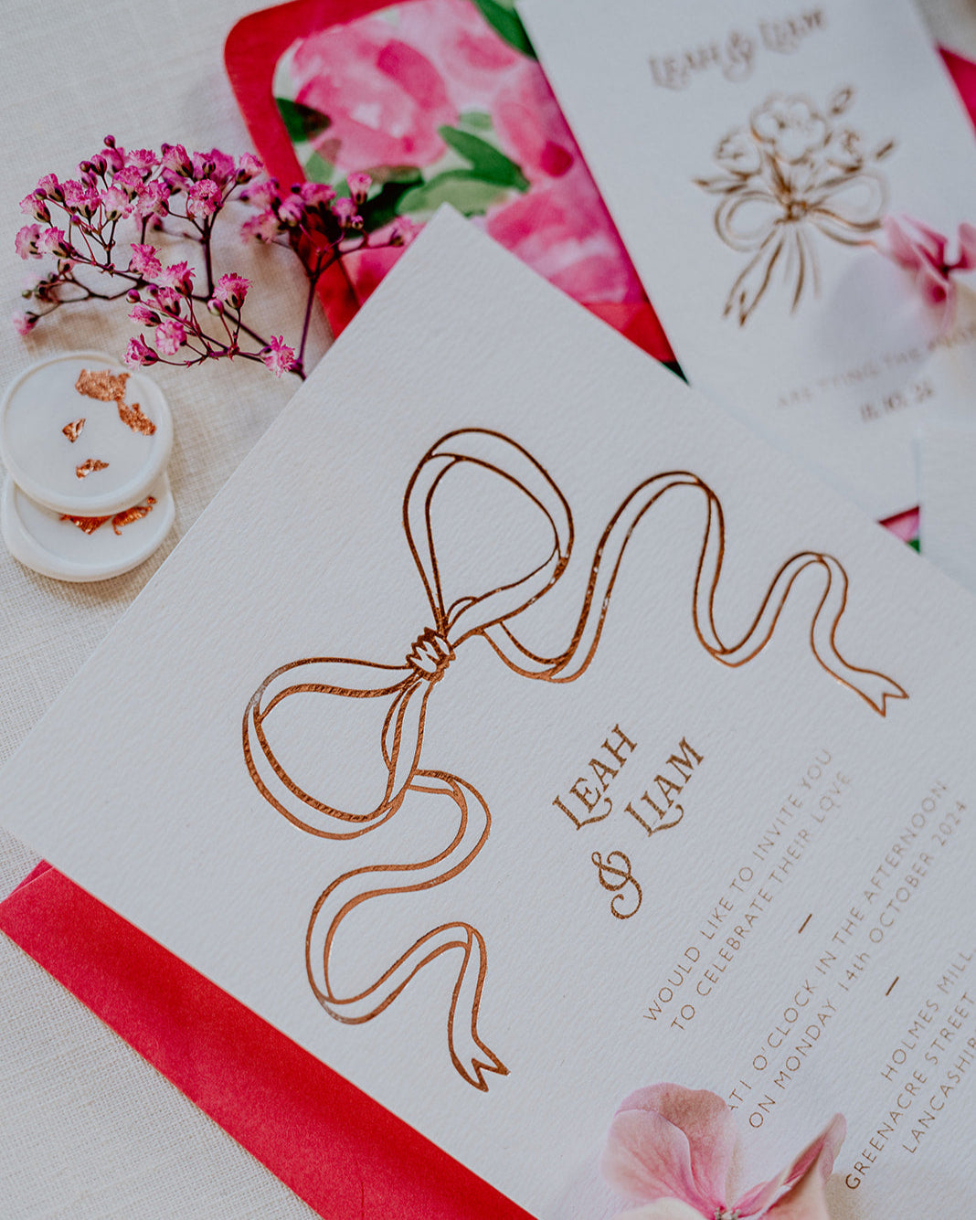 Close up of a wedding Invitation featuring a large Rose Gold Bow Design, foiled onto  thick textured card with couples names and information printed in a soft brown colour. Paired with hot pink envelope with floral envelope liner, white wax seal with rose gold flakes. Designed by Fancy Folk Wedding Stationery