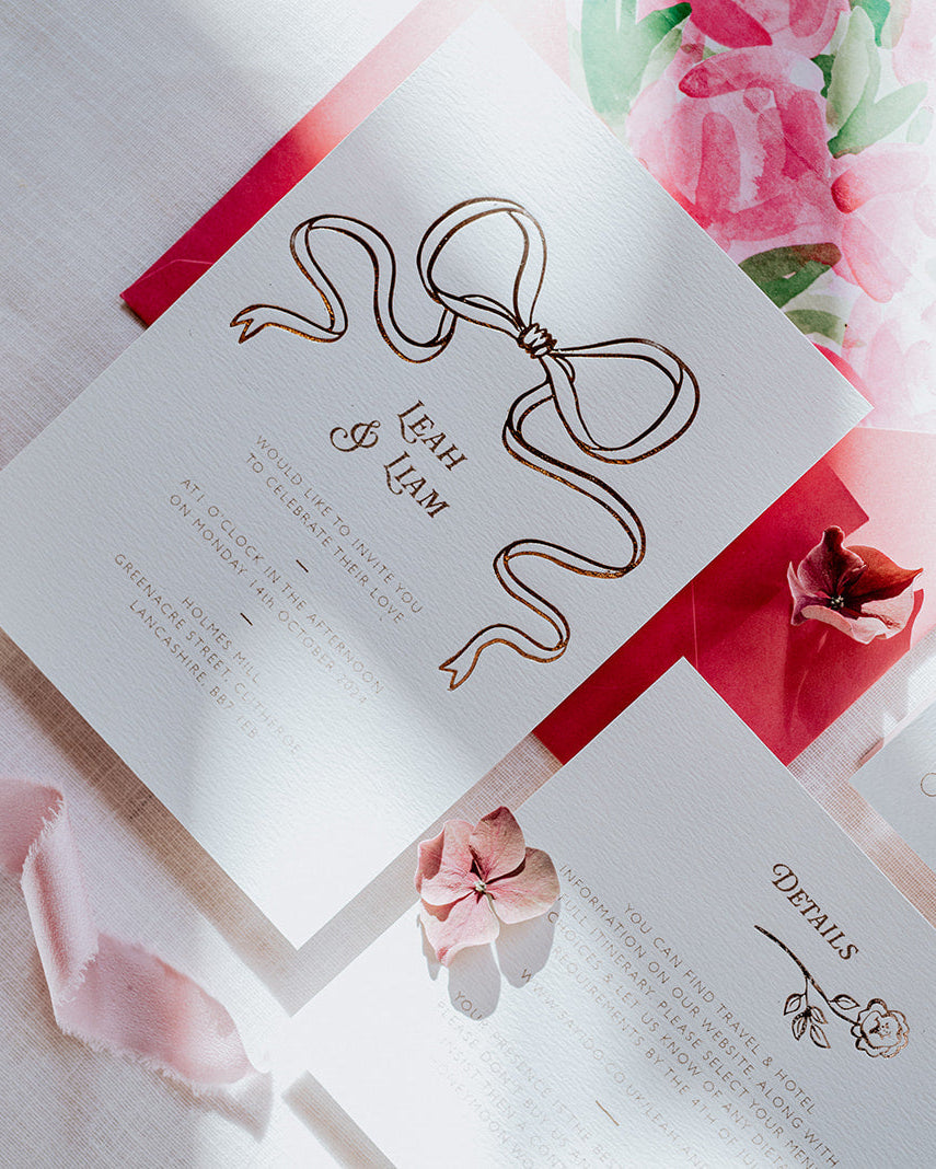 Bow Wedding Invitation Suite featuring a large Rose Gold Bow Design. Foiled onto thick textured card with couples names and information printed in a soft brown colour. Paired with hot pink envelope with floral envelope liner, white wax seal with rose gold flakes and blush pink silk ribbon. Laid out flat lay style with Details card and RSVP. Designed by Fancy Folk Wedding Stationery