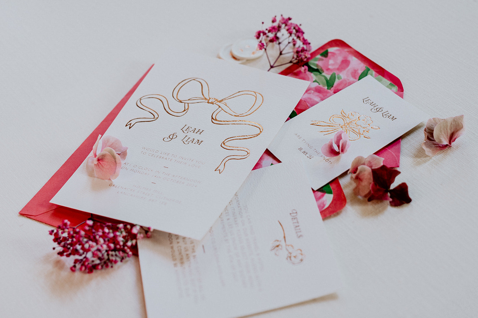 Bow Wedding Invitation Suite featuring a large Rose Gold Bow Design, foiled onto  thick textured card with couples names and information printed in a soft brown colour. Paired with hot pink envelope with floral envelope liner, white wax seal with rose gold flakes and blush pink silk ribbon. Laid out flat lay style with Details card and RSVP. Designed by Fancy Folk Wedding Stationery