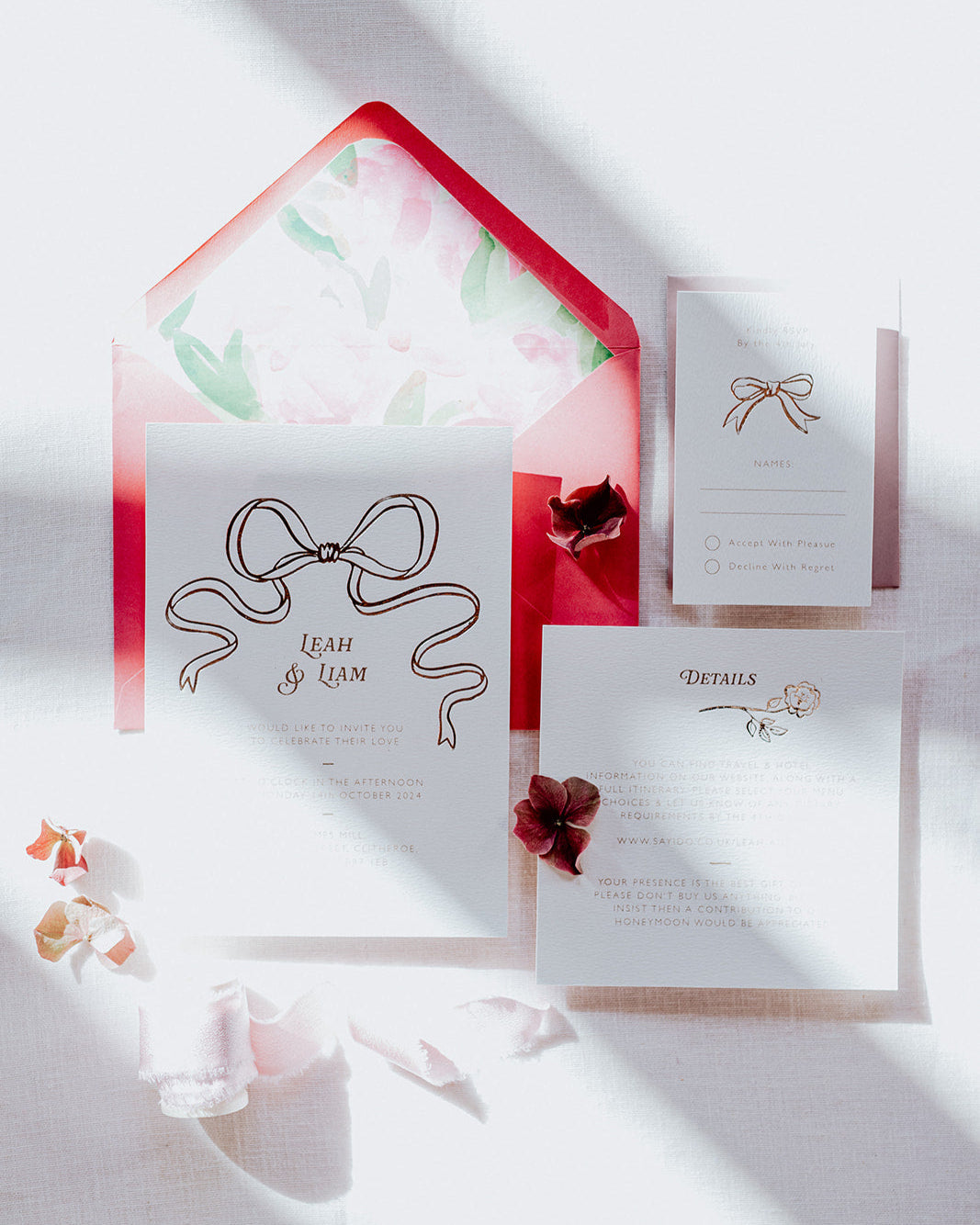 Wedding Invitation Sample Pack featuring a large Rose Gold Bow Design, foiled onto  thick textured card with couples names and information printed in a soft brown colour. Paired with hot pink envelope with floral envelope liner, white wax seal with rose gold flakes and blush pink silk ribbon. Laid out flat lay style with Details card and RSVP. Designed by Fancy Folk Wedding Stationery