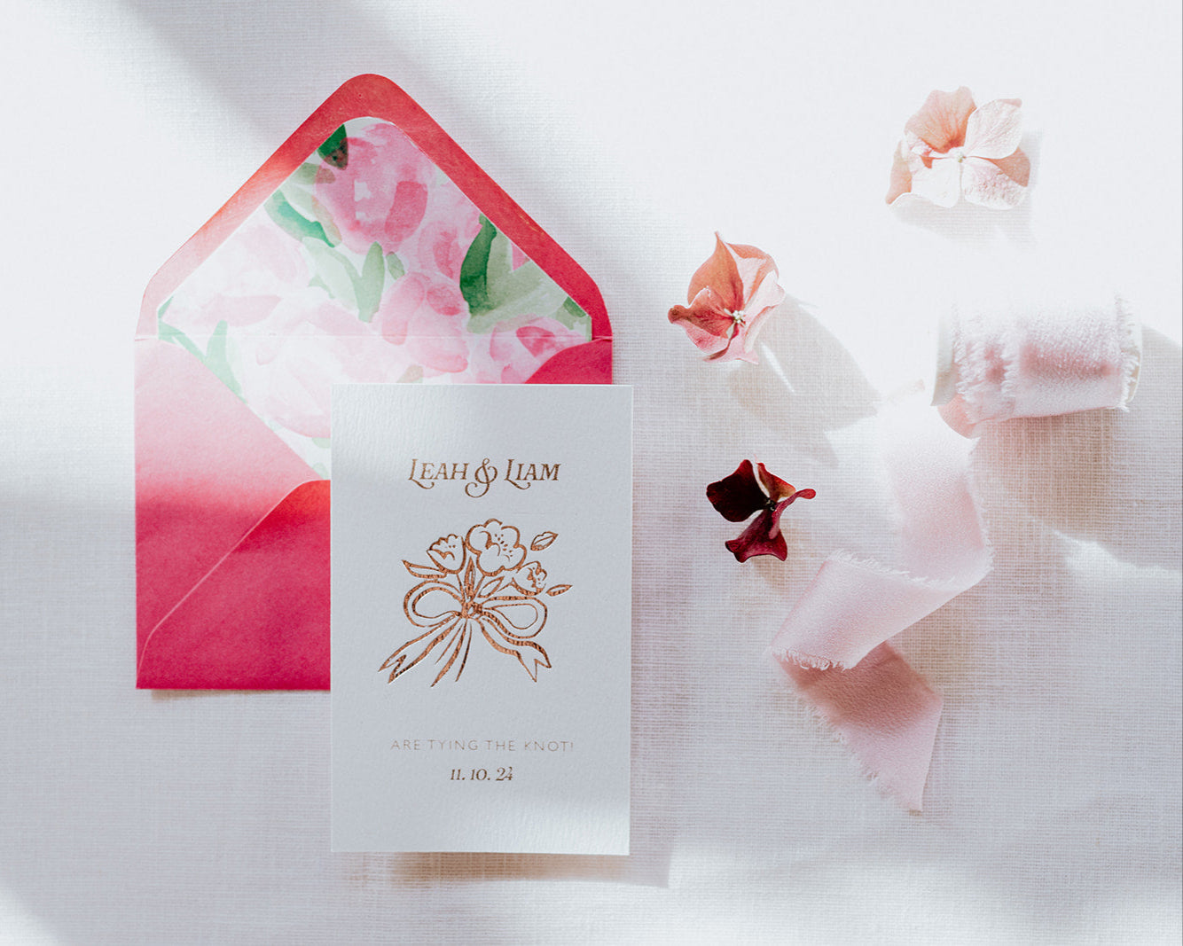 Bow Posy Wedding Save The Date Card with Hot Pink floral envelope liners. Hot foil printed onto thick GFSmith Card with couples names and wedding date. "Leah & Liam are tying the knot! 11.10.24" Designed by Fancy Folk Wedding Stationery.
