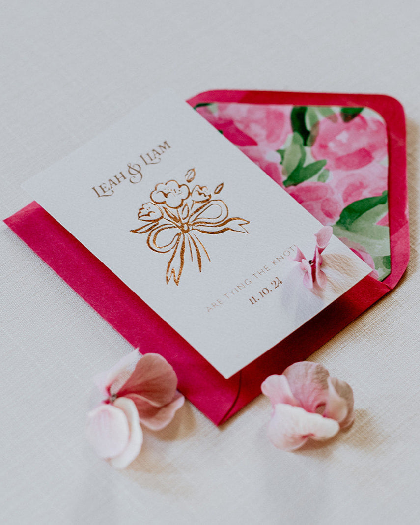 Bow Posy Wedding Save The Date Card with Hot Pink floral envelope liners. Hot foil printed onto thick GFSmith Card with couples names and wedding date. "Leah & Liam are tying the knot! 11.10.24" Designed by Fancy Folk Wedding Stationery. 