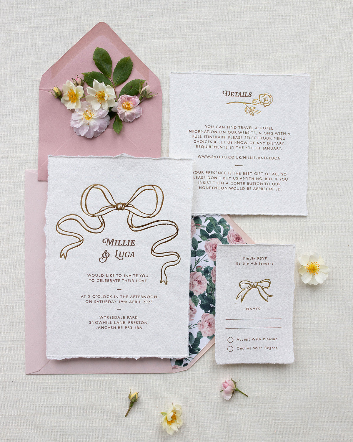 Bridgerton Inspired Gold Foil Bow design wedding invitation suite. Dusky pink envelope paired with floral rose garden envelope liner. Matching Details card and RSVP cards. Printed on a luxurious and tactile handmade cotton paper. Flat lay styled  with wild roses. Designed by Fancy Folk Weddings