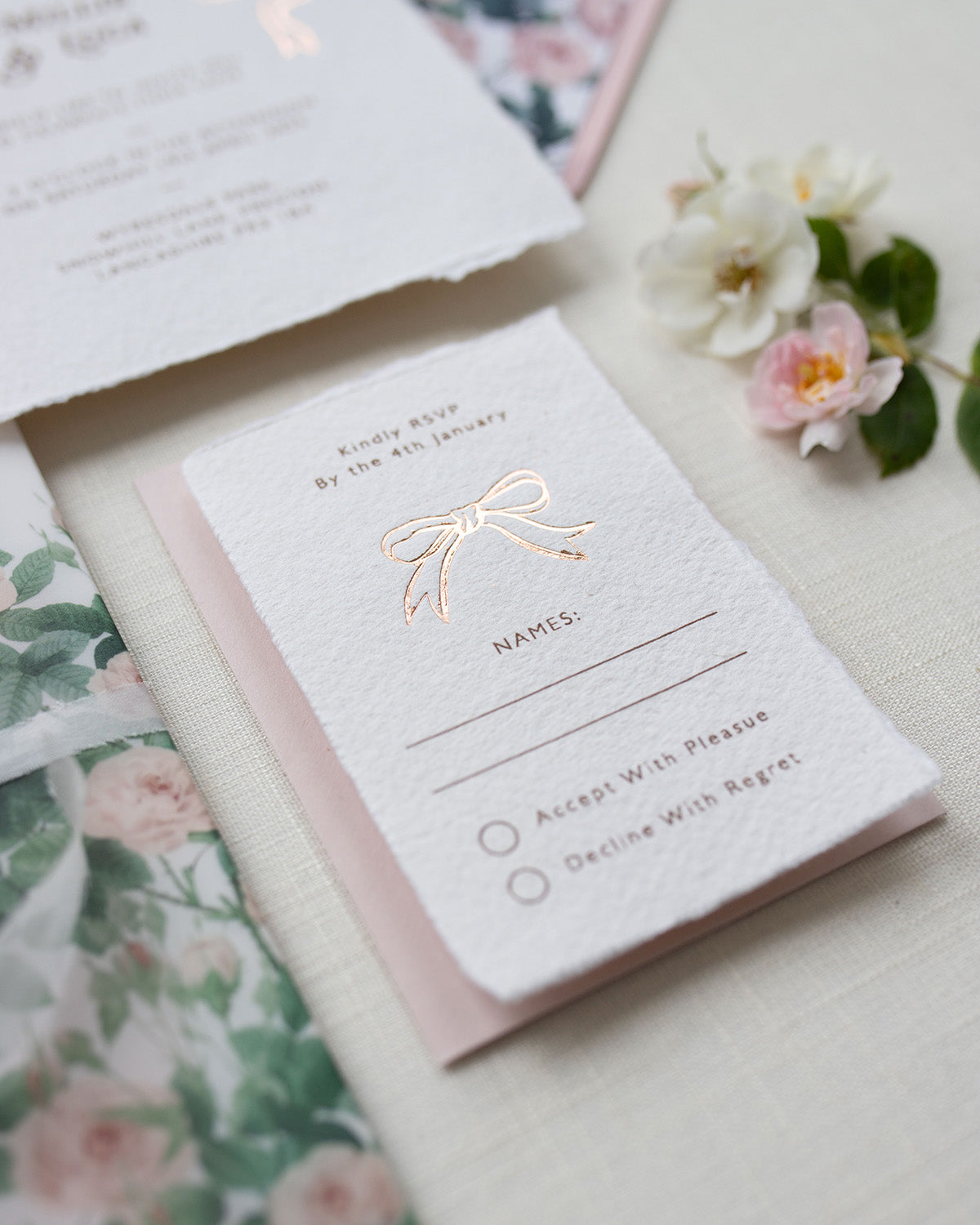 Close up of Rose gold Bow wedding RSVP card. Paired with blush pink coloured envelope. Printed on luxury hand made cotton paper with romantic hand torn edges. Designed by Fancy Folk Weddings