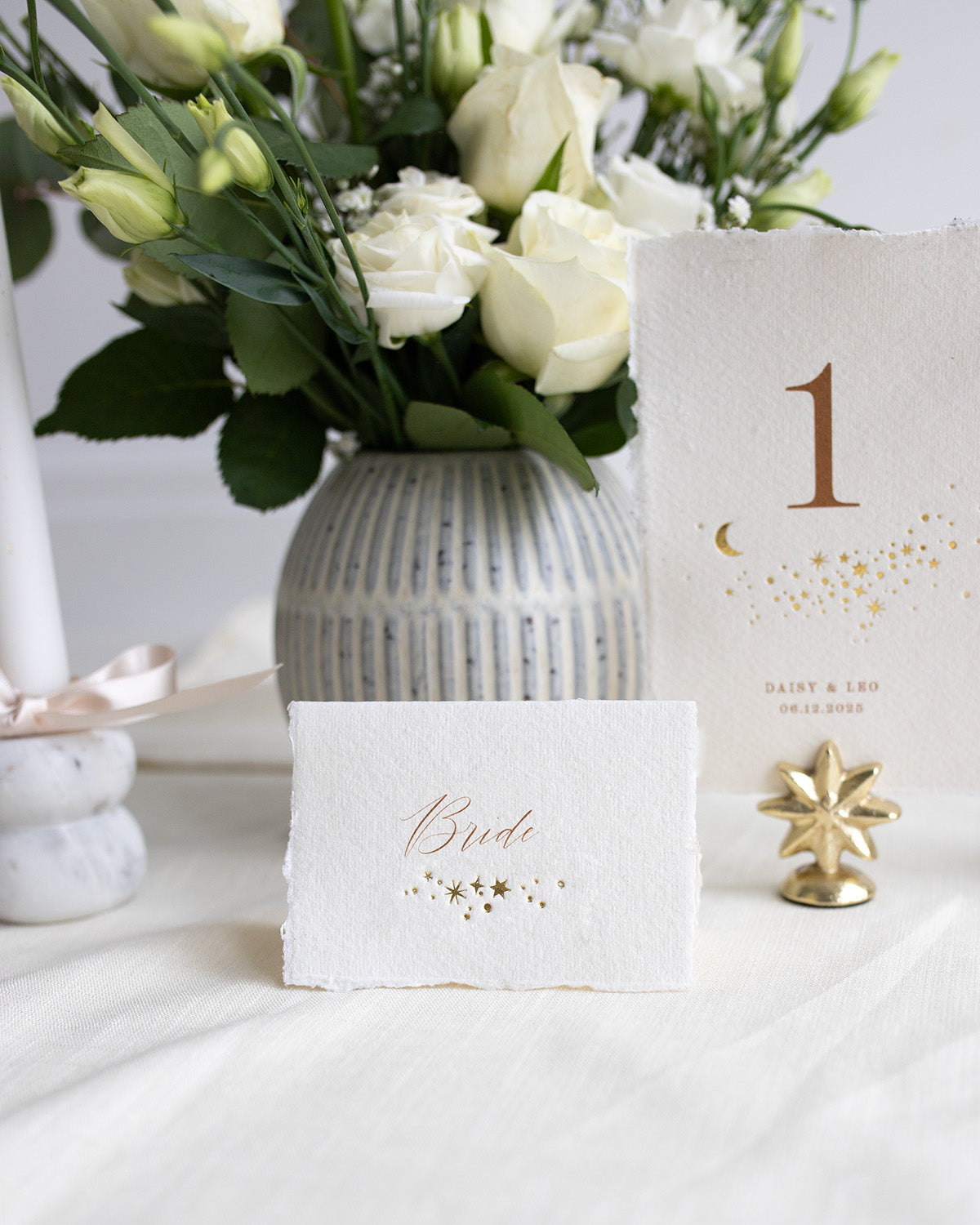 Celestial wedding place card. Gold foil star constellation with printed name above, reads "Bride". Foiled onto handmade paper with a beautiful romantic hand torn edge. Styled with white florals and neutral linens. Fancy Folk