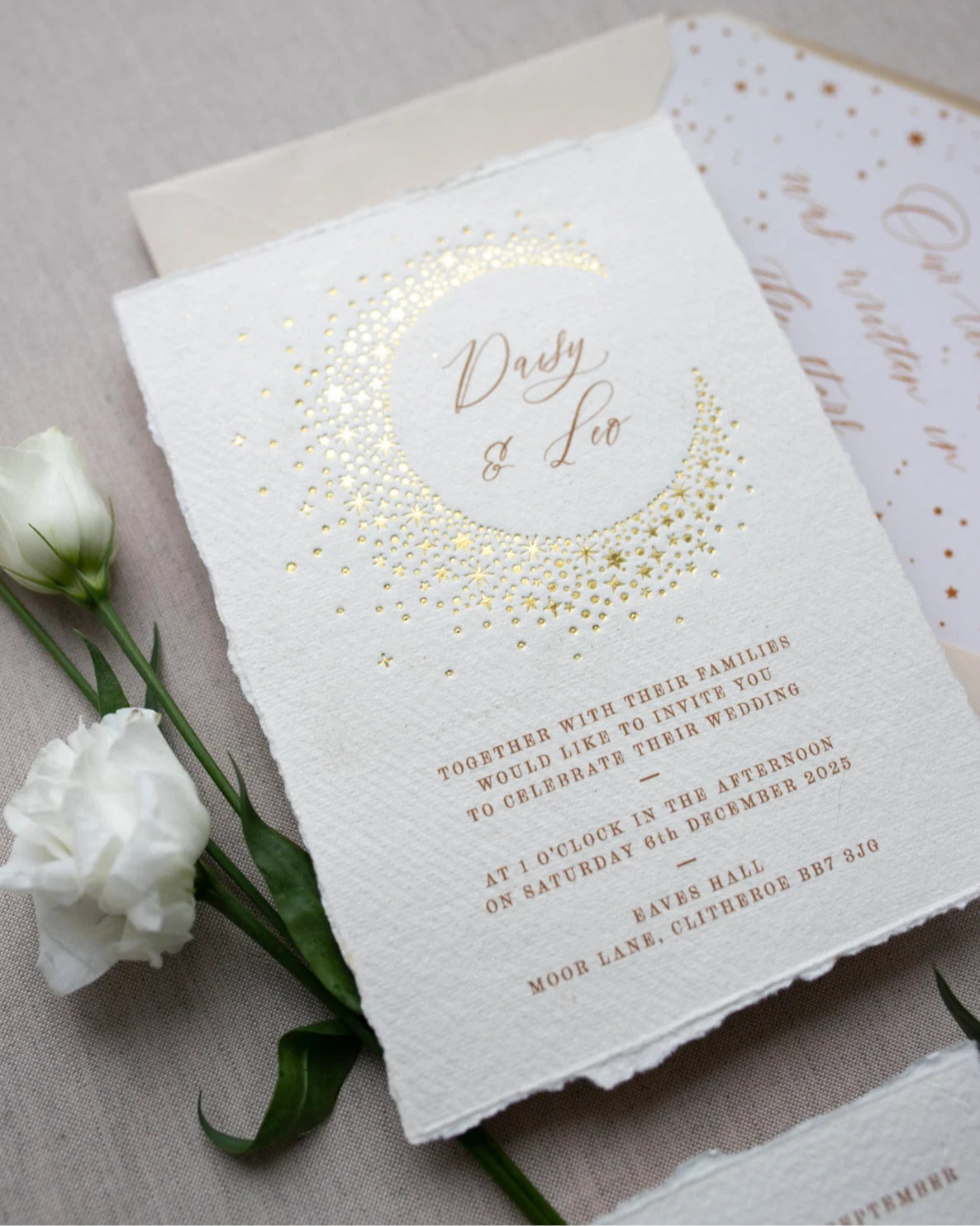 Celestial themed wedding invitation and almond coloured envelope. A truly magical crescent moon design made up of lots of little stars is hot foiled in gold on to tactile handmade paper with a torn romantic edge. The gold foil sparkles in the light. Luxury envelope liner reads "Our love was written I the stars". FancyFolk Design