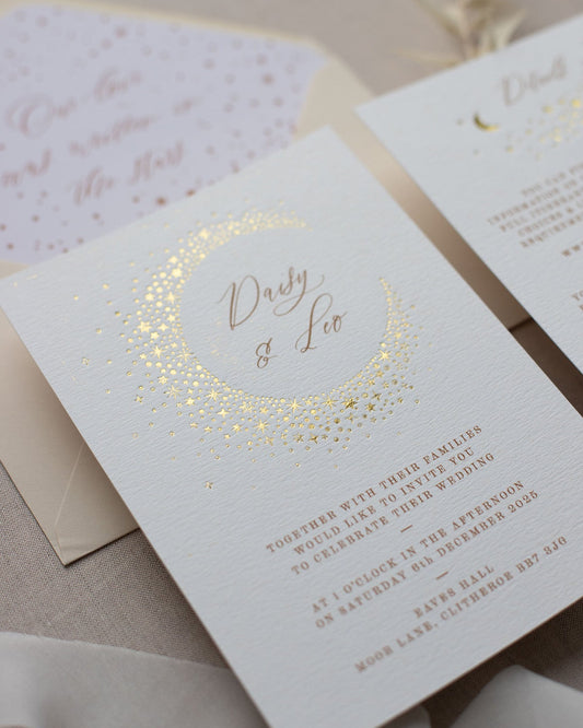 Celestial themed wedding invitation. A truly magical crescent moon design made up of lots of little stars is hot foiled in gold on to the main invitation. The invitations are foiled and printed onto thick textured card, styled with almond coloured envelopes. Fancy Folk Design