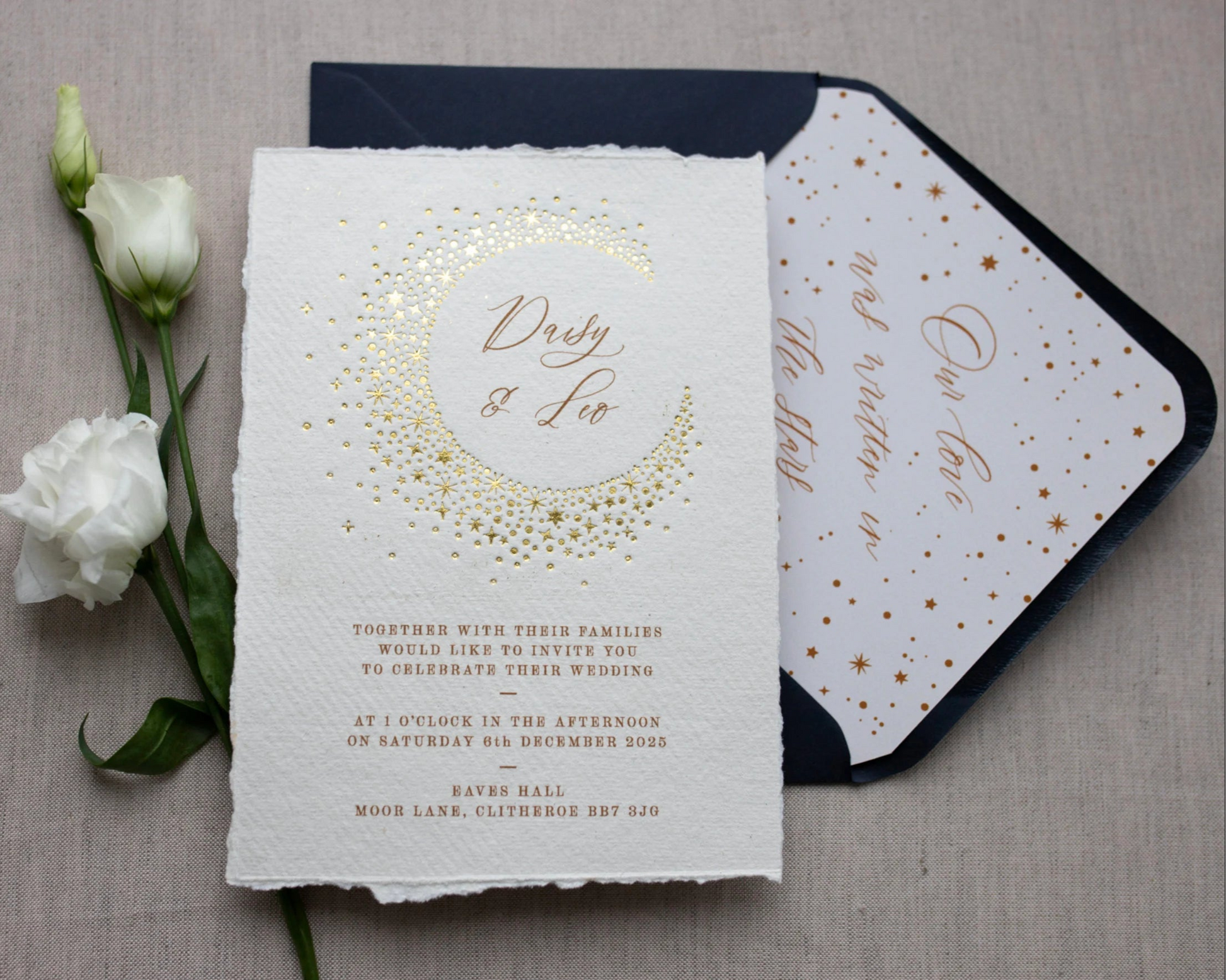 Celestial themed wedding invitation and navy blue envelope. A truly magical crescent moon design made up of lots of little stars is hot foiled in gold on to tactile handmade paper with a torn romantic edge. The gold foil sparkles in the light. Luxury envelope liner reads "Our love was written I the stars". FancyFolk Design