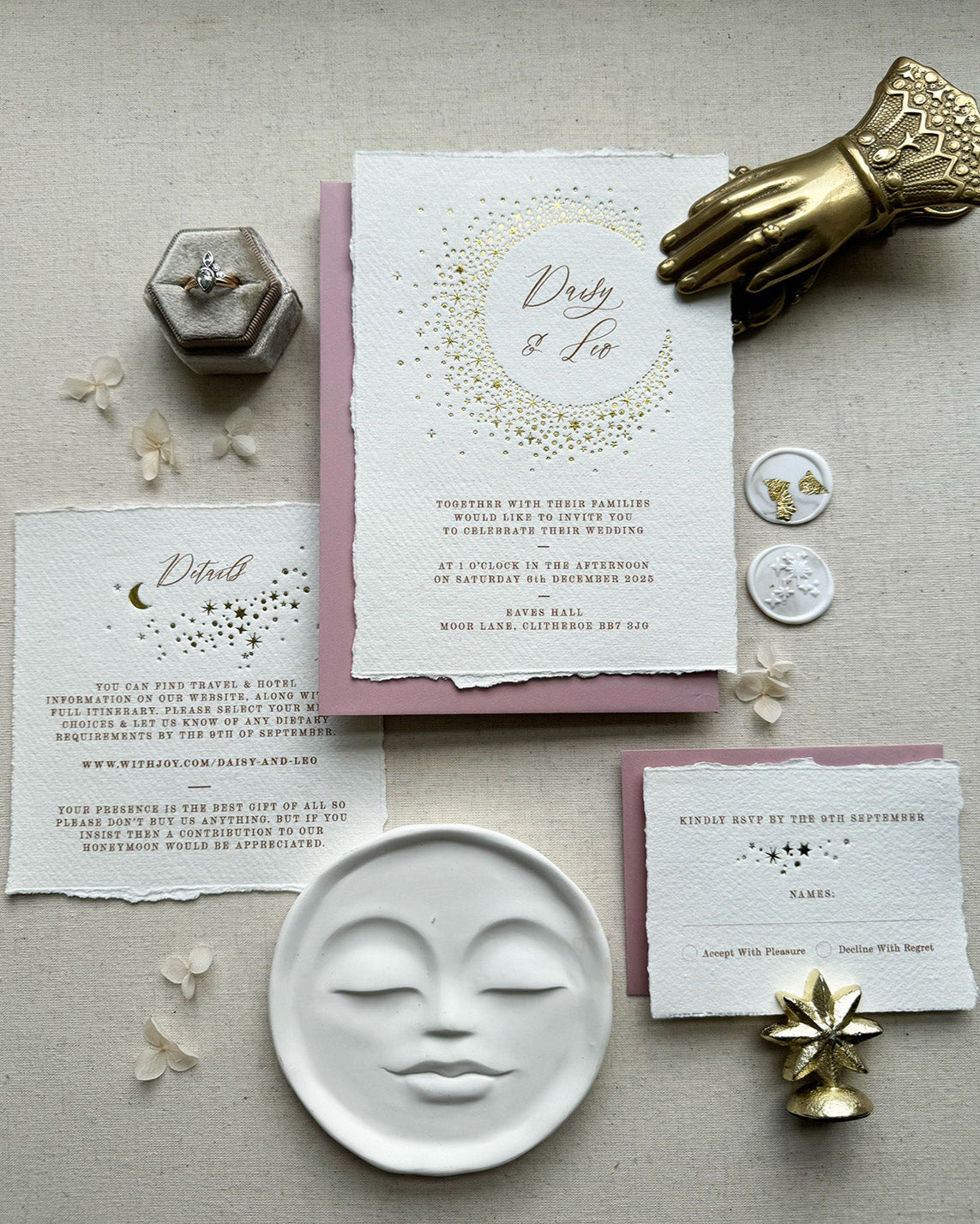Celestial themed wedding stationery suite laid out in a flat lay format. A truly magical crescent moon design made up of lots of little stars is hot foiled in gold on to the main invitation. Smaller cluster of gold stars feature on the details card and RSVP. The invitations are foiled and printed onto tactile handmade paper with a torn romantic edge. Styled with dusky Pink envelopes and gold leaf wax seals. FancyFolk Design