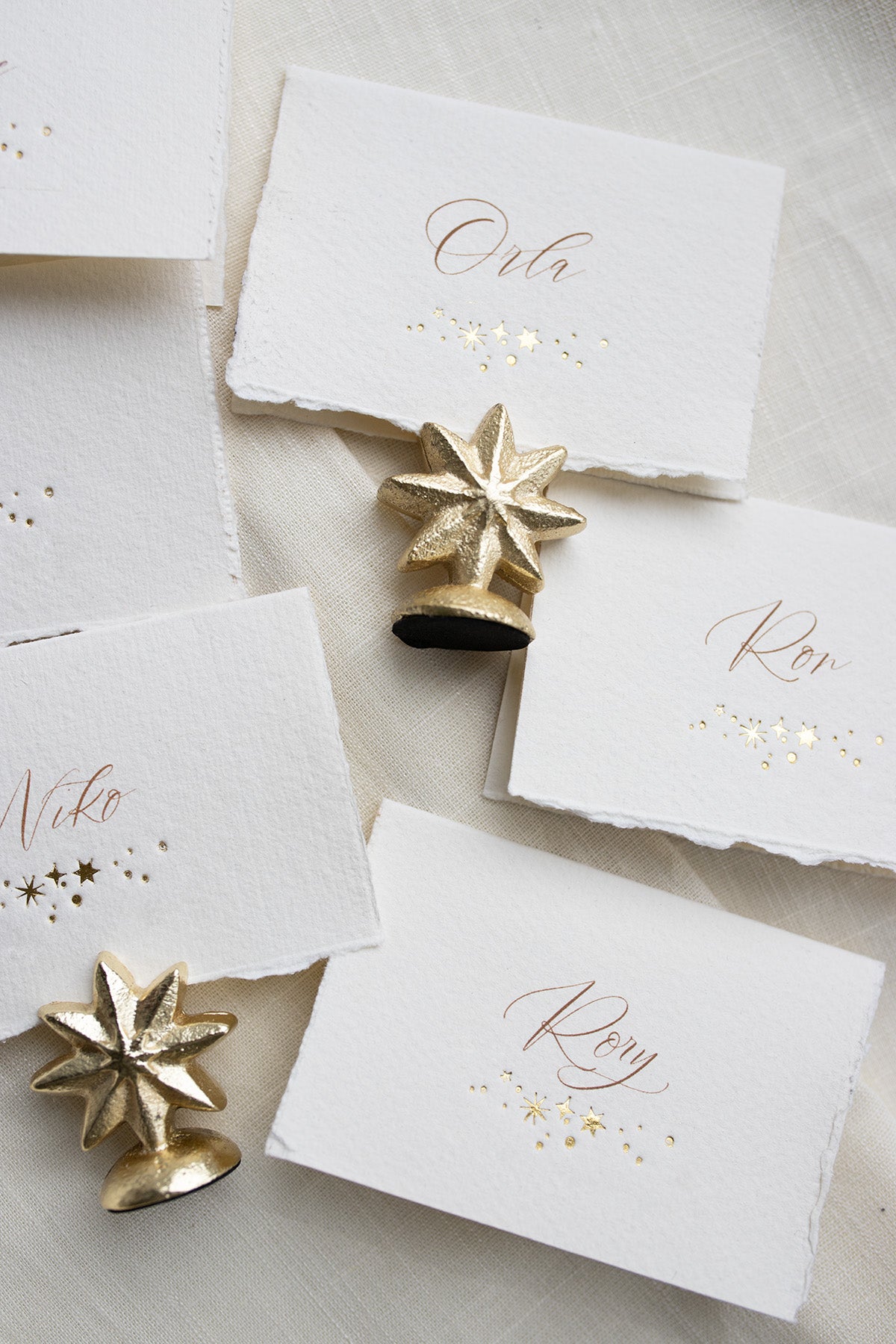 Celestial wedding place card. Gold foil star constellation with printed name above. Foiled onto handmade paper with a beautiful romantic hand torn edge. Styled with  neutral linens and gold star shaped card holder. Fancy Folk