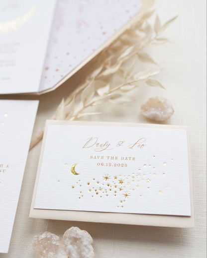 A Celestial Wedding Save the date card with gold stars and mood design. Stars are scattered across the card and  foiled in gold onto thick textured off white card. With text printed above reading "Daisy & Leo Save the Date " styled with neutral almond coloured envelope. Fancy Folk Design.