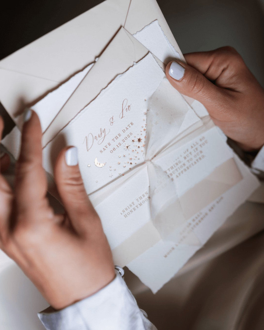 A lady opening up a wedding sample pack, tied with neutral silk ribbon. Celestial wedding save the date card stacked on top. Gold foil moon and stars design is embossed onto handmade paper with torn edges. Almond envelopes. Fancy Folk