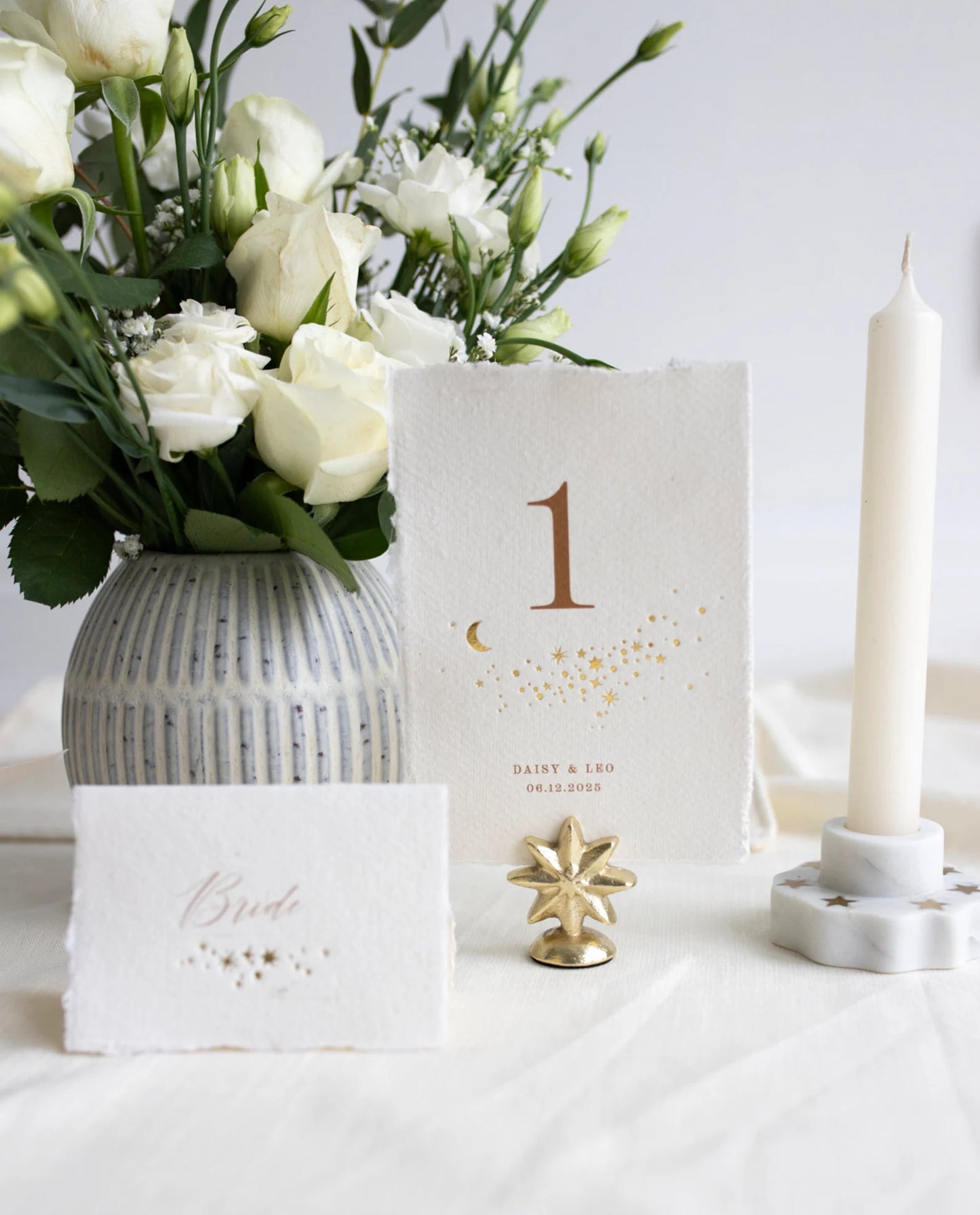 Celestial themed design featuring a scatter of gold stars and a little moon. Gold hot foiled onto handmade cotton paper with torn edges.Printed number and coupled names and wedding date below. Styled with white florals, neutral linens and gold star shaped card. Fancy Folk Design