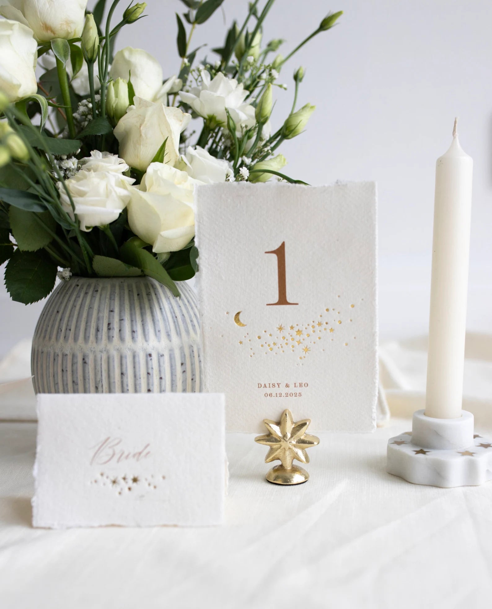 Celestial themed design featuring a scatter of gold stars and a little moon. Gold hot foiled onto handmade cotton paper with torn edges.Printed number and coupled names and wedding date below. Styled with white florals, neutral linens and gold star shaped card. Fancy Folk Design