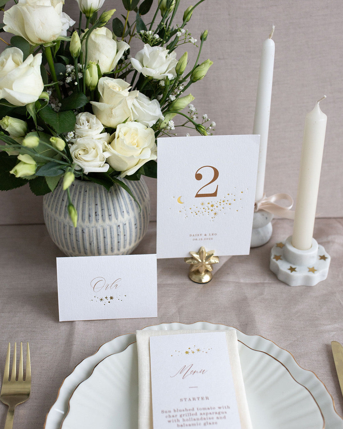 Celestial Wedding menu, featuring a little constellation of gold foil stars at the top and printed menu information below. Styled placed on top of a neutral napkin on beautiful crockery with gold gilding. This menu is foiled not thick textured card. Fancy Folk