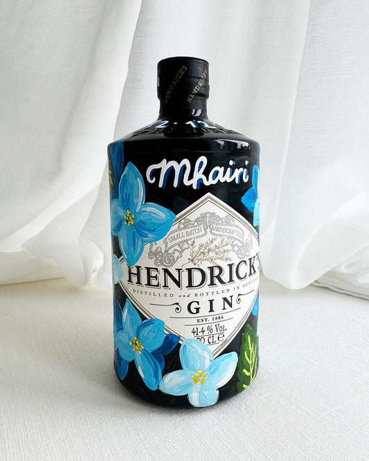 Hand painted Occasion Bottle. Blue Hydrangeas in different shades are painted all around the bottle. Calligraphy name of the recipient at the front of the bottle in white. Gold leaf accents to finish. Fancy Folk Design