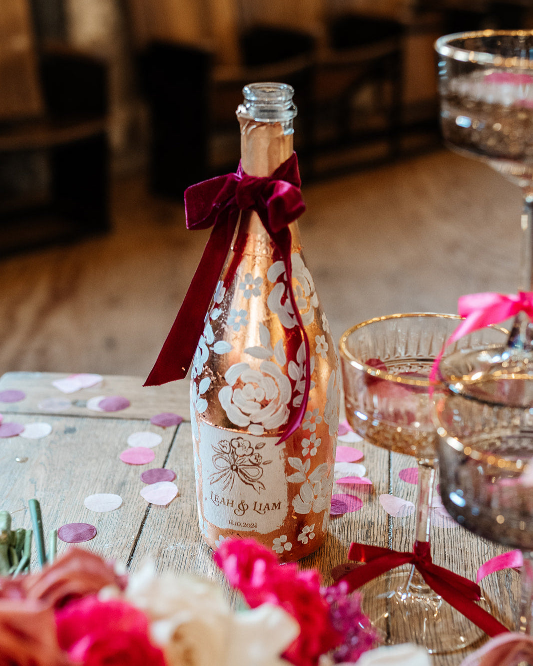 Hand painted wedding Champagne Bottle. Lux Copper leaf base with white painted roses all around the bottle. Personalise label with couples names and wedding date. Perfect for a champagne tower moment. By Fancy Folk Design