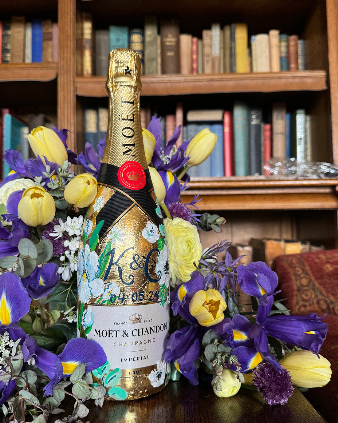 Hand painted Bottle of Moet Champagne. Perfect wedding gift with couples monogram initials and wedding date. Gold leaf base painted florals to match the bridal bouquet. Woman's hands holding the bottle. Fancy Folk Design