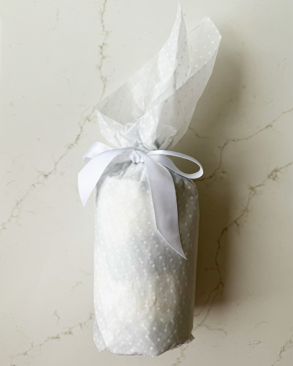 Bottle wrapped in tissue and tied in a pretty bow with white ribbon.