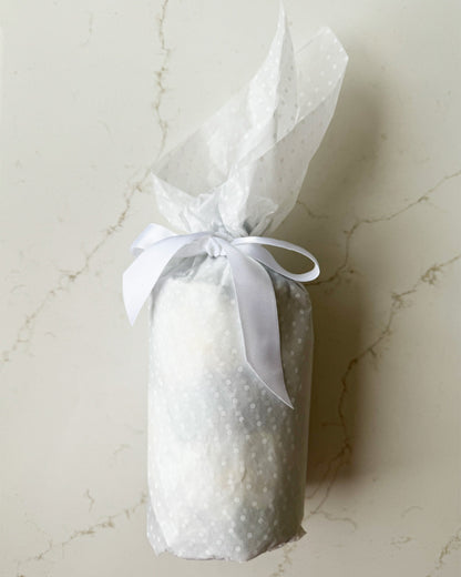 Bottle wrapped in tissue and tied in a pretty bow with white ribbon.