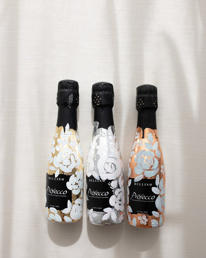 Mini bottles of Prosecco hand painted with a white roses design on a metallic base. Gold, silver and copper examples of the same design. The perfect luxury bridesmaid proposal gift. Fancy Folk Design