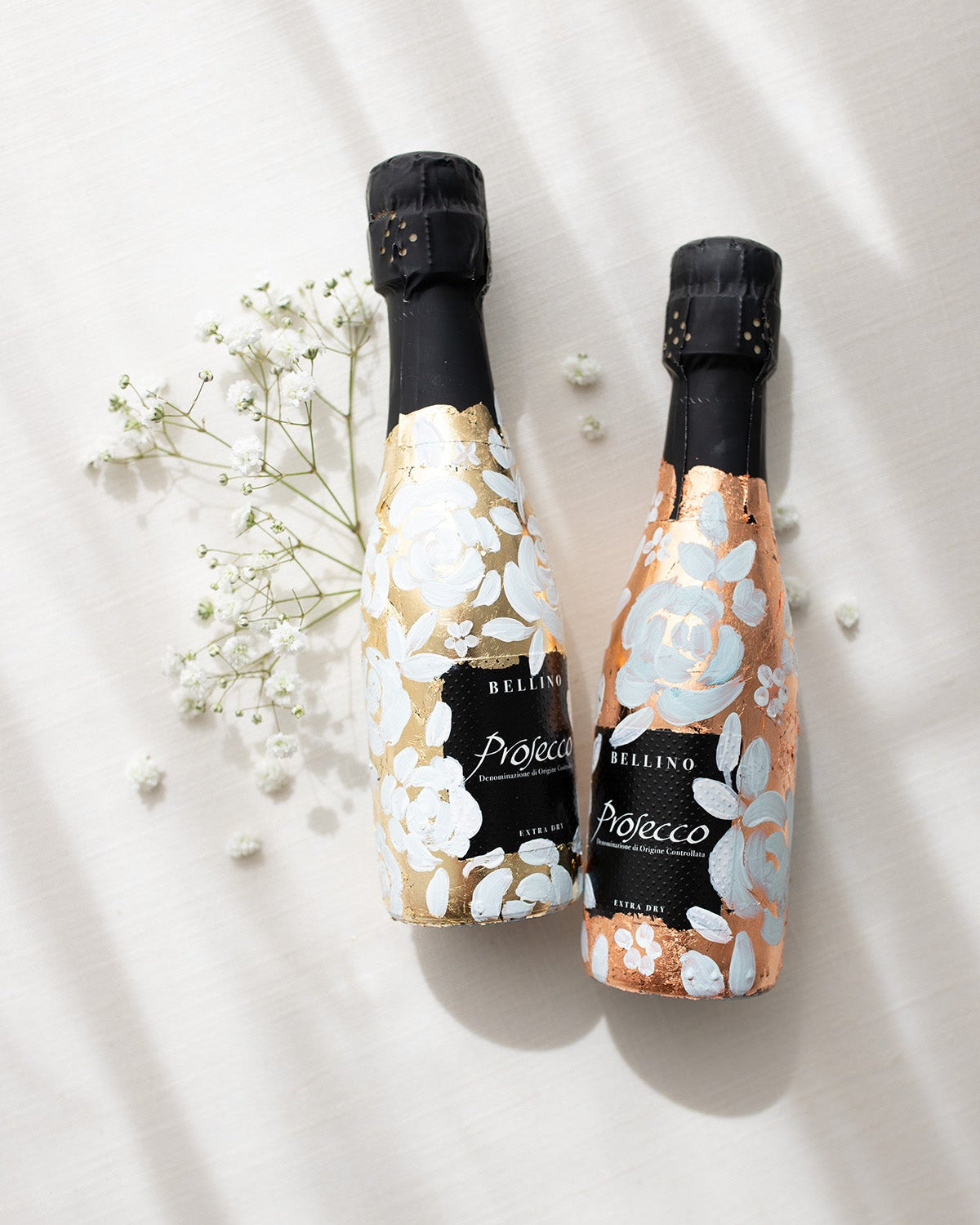 Mini bottles of Prosecco hand painted with a white roses design on a metallic base. Gold and copper examples of the same design. The perfect luxury bridesmaid proposal gift. Fancy Folk Design