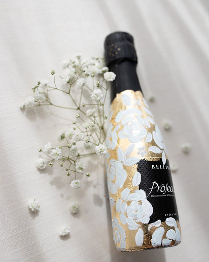 Mini bottles of Prosecco hand painted with a white roses design on a metallic gold base. The perfect luxury bridesmaid proposal gift. Fancy Folk Design